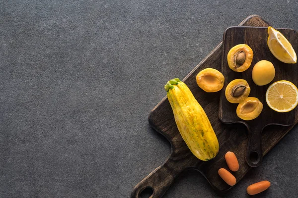 Ansicht von gelbem Obst und Gemüse auf hölzernen Schneidebrettern auf grauem strukturiertem Hintergrund mit Kopierraum — Stockfoto