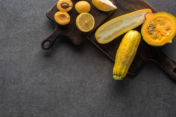 Vista superior de frutas y verduras amarillas en tablas de cortar de madera sobre fondo texturizado gris con espacio para copiar - foto de stock