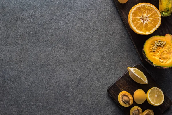 Top view of yellow fruits and vegetables on wooden cutting boards on grey textured background with copy space — Stock Photo