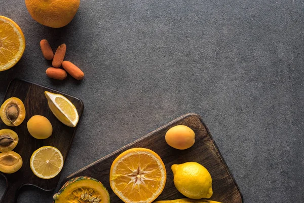 Top view of yellow fruits and vegetables on wooden cutting boards on grey textured background with copy space — Stock Photo