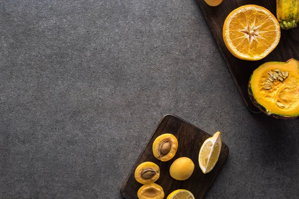 Top view of yellow fruits and vegetables on wooden cutting boards on grey textured background with copy space — Stock Photo