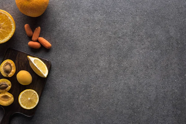 Vista superior de frutas y verduras amarillas sobre tabla de cortar de madera sobre fondo texturizado gris con espacio para copiar - foto de stock