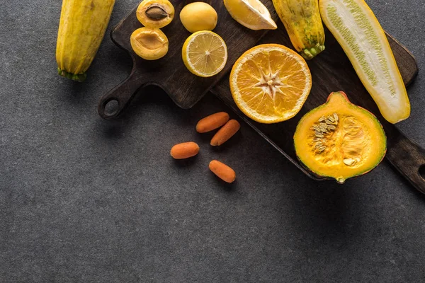 Vista superior de frutas y verduras amarillas en tablas de cortar de madera sobre fondo texturizado gris con espacio para copiar - foto de stock