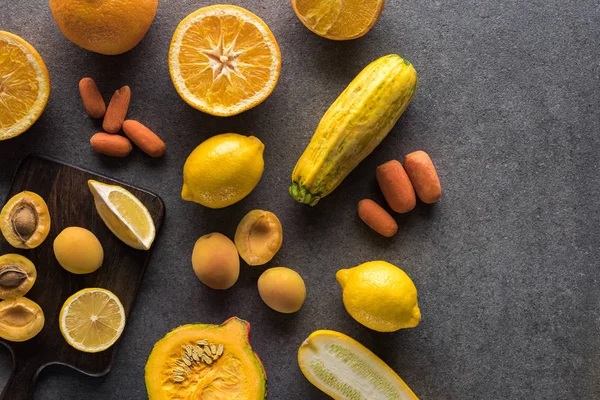 Draufsicht auf gelbes Obst und Gemüse und hölzerne Schneidebretter auf grauem Hintergrund — Stockfoto