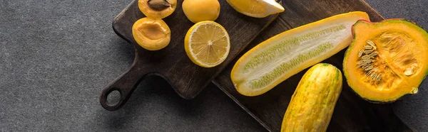 Vista superior de frutas y verduras amarillas en tablas de cortar de madera sobre fondo texturizado gris, plano panorámico - foto de stock