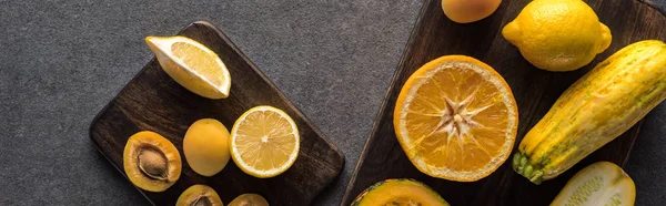 Top view of yellow fruits and vegetables on wooden cutting boards on grey textured background, panoramic shot — Stock Photo