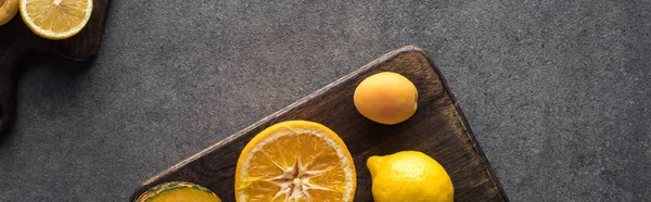 Top view of yellow fruits on wooden cutting boards on grey textured background, panoramic shot — Stock Photo