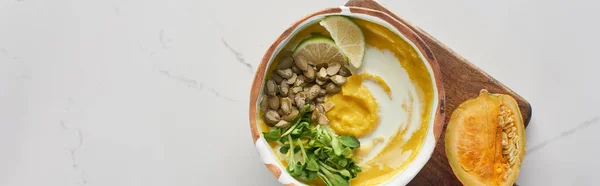 Top view of autumnal mashed pumpkin soup in bowl on wooden cutting board with pumpkin on marble surface, panoramic shot — Stock Photo