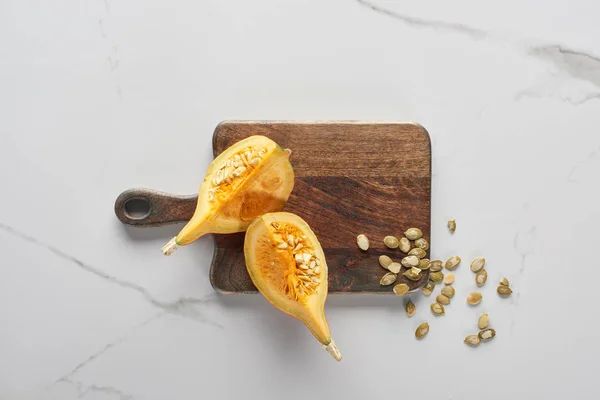 Vue du dessus de la planche à découper en bois avec citrouille et graines sur la surface du marbre — Photo de stock