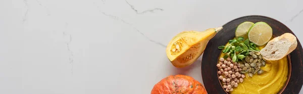 Vista dall'alto di purè di zucca autunnale minestra in ciotola vicino a zucca su superficie di marmo, colpo panoramico — Foto stock