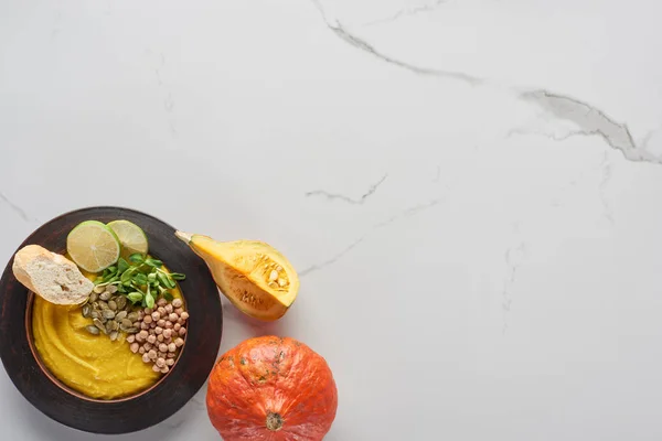 Top view of autumnal mashed pumpkin soup in bowl near pumpkin on marble surface — Stock Photo