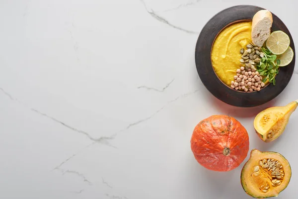 Top view of autumnal mashed pumpkin soup in bowl near pumpkin on marble surface — Stock Photo