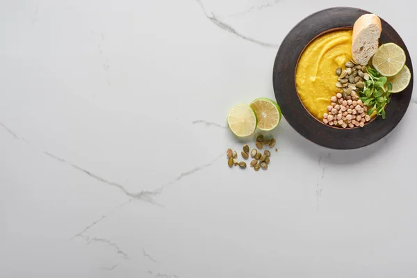 Vue du dessus de la soupe automnale à la purée de citrouille dans un bol près des graines de citrouille et de la chaux sur la surface du marbre — Stock Photo