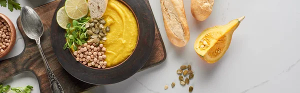 Top view of autumnal mashed pumpkin soup in bowl on wooden cutting board on marble surface, panoramic shot — Stock Photo