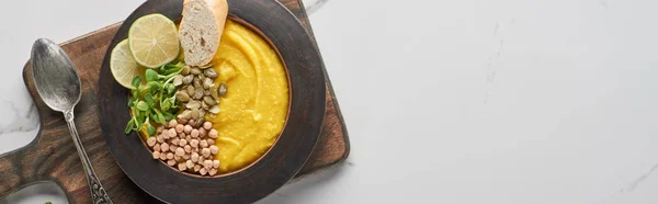 Top view of autumnal mashed pumpkin soup in bowl on wooden cutting board with spoon on marble surface, panoramic shot — Stock Photo