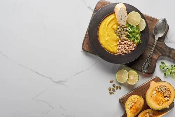 Vue du dessus de la soupe de citrouille en purée automnale dans un bol sur une planche à découper en bois sur une surface en marbre — Photo de stock