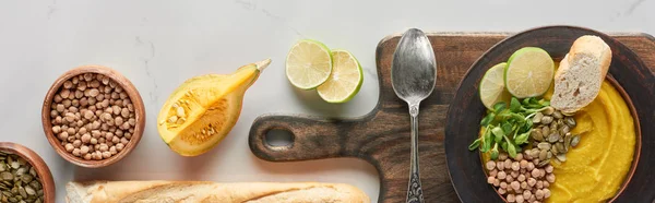 Vue du dessus de la soupe de citrouille en purée automnale dans un bol sur une planche à découper en bois à la surface du marbre, vue panoramique — Photo de stock