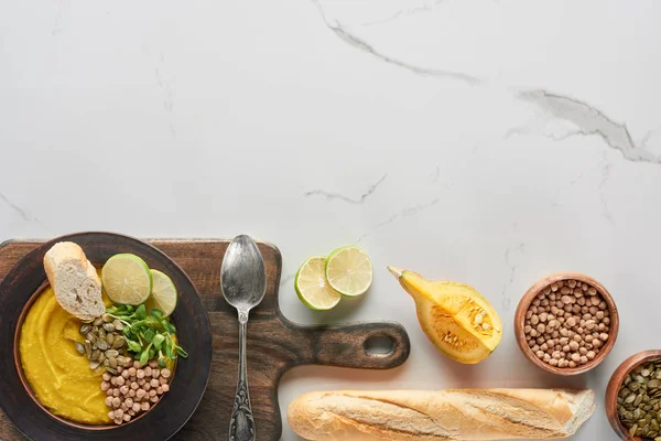 Vista superior de la sopa de calabaza molida otoñal en un tazón en una tabla de cortar de madera cerca del pan en una superficie de mármol - foto de stock