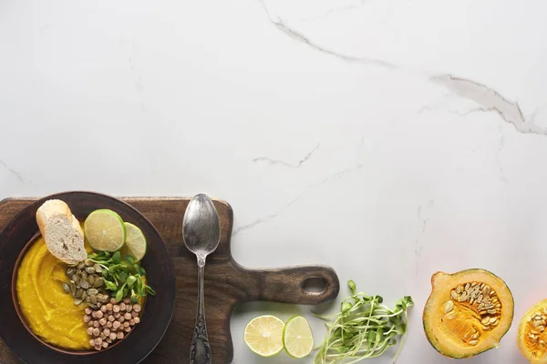 Top view of autumnal mashed pumpkin soup in bowl on wooden cutting board with spoon on marble surface — Stock Photo