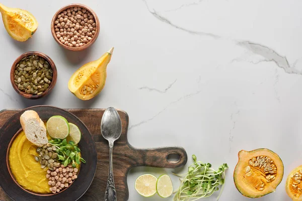 Vue du dessus de la soupe automnale à la citrouille écrasée dans un bol sur une planche à découper en bois avec cuillère sur une surface en marbre — Photo de stock