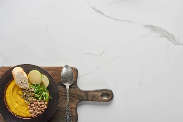 Vue du dessus de la soupe automnale à la citrouille écrasée dans un bol sur une planche à découper en bois avec cuillère sur une surface en marbre — Photo de stock