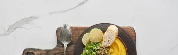 Top view of autumnal mashed pumpkin soup in bowl on wooden cutting board with spoon on marble surface, panoramic shot — Stock Photo