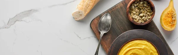 Top view of autumnal mashed pumpkin soup near bread and pumpkin seeds on marble surface, panoramic shot — Stock Photo