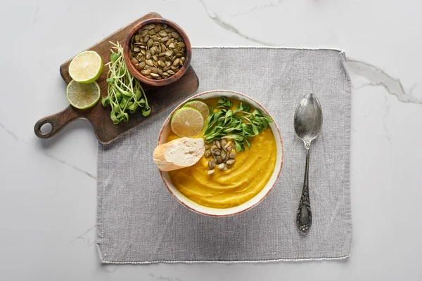 Top view of autumnal mashed pumpkin soup ion napkin with spoon near ingredients on marble surface — Stock Photo