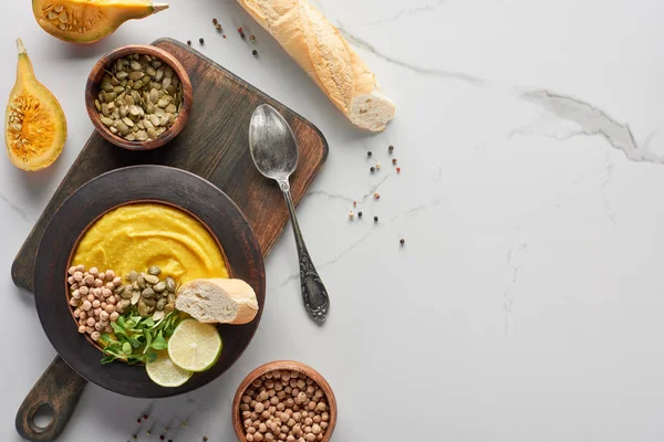 Vue de dessus de la soupe de citrouille en purée automnale sur planche à découper en bois avec cuillère et ingrédients sur la surface du marbre — Photo de stock