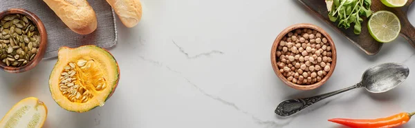 Top view of pumpkin, seeds, silver spoon, bread and chickpea on marble surface, panoramic shot — Stock Photo