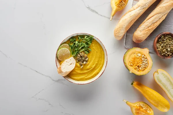 Top view of autumnal mashed pumpkin soup in bowl near bread on marble surface — Stock Photo