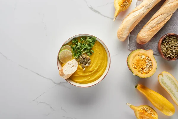 Vue du dessus de la purée automnale de soupe de citrouille dans un bol près du pain sur la surface du marbre — Photo de stock