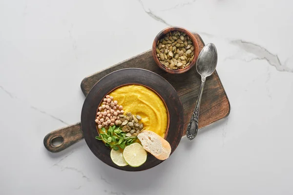 Top view of autumnal mashed pumpkin soup on wooden cutting board with seeds and spoon on marble surface — Stock Photo