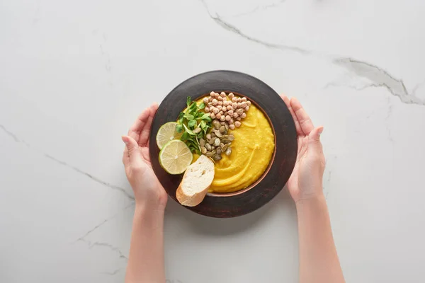 Cropped view of woman holding autumnal mashed pumpkin soup on marble surface — Stock Photo