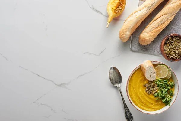 Top view of autumnal mashed pumpkin soup near silver spoon and bread on marble surface — Stock Photo