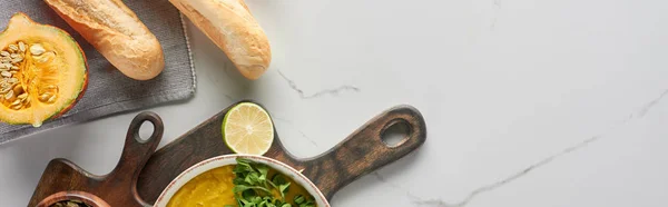 Vista superior de sopa de calabaza molida otoñal en tabla de cortar de madera en la superficie de mármol cerca del pan — Stock Photo