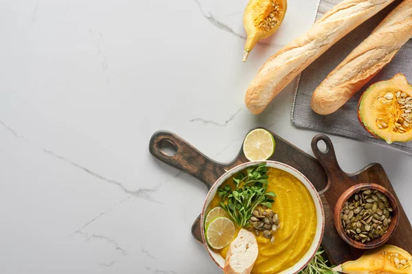 Vista superior de sopa de calabaza molida otoñal sobre tabla de cortar de madera cerca de baguette en superficie de mármol - foto de stock