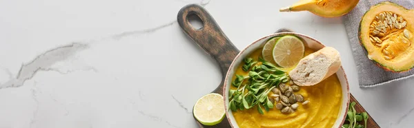 Panoramic shot of autumnal mashed pumpkin soup on wooden cutting board on marble surface — Stock Photo