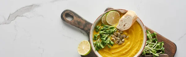 Top view of autumnal mashed pumpkin soup on wooden cutting board on marble surface, panoramic shot — Stock Photo