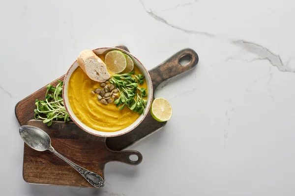 Top view of autumnal mashed pumpkin soup on wooden cutting board on marble surface with silver spoon — Stock Photo