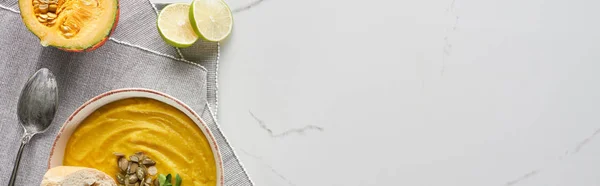 Top view of autumnal mashed pumpkin soup on marble surface near silver spoon and lime, panoramic shot — Stock Photo