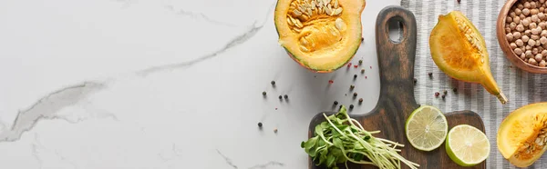 Top view of wooden cutting board with pumpkin, lime and sprouts on marble surface, panoramic shot — Stock Photo