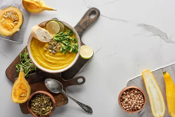 Vista superior da sopa de abóbora triturada sazonal na placa de corte de madeira com ingredientes na superfície de mármore — Fotografia de Stock