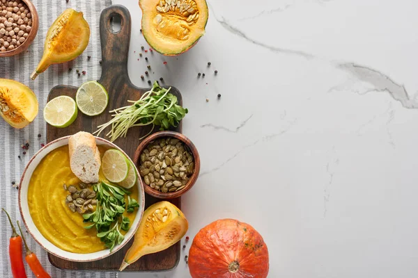 Top view of seasonal mashed pumpkin soup on wooden cutting board with ingredients on marble surface — Stock Photo