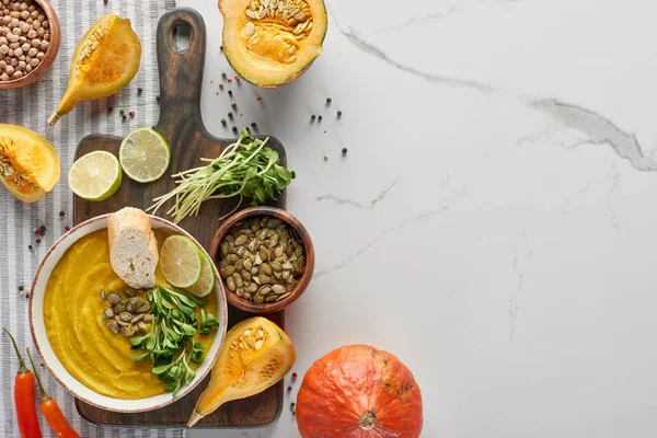 Vista superior da sopa de abóbora triturada sazonal na placa de corte de madeira com ingredientes na superfície de mármore — Fotografia de Stock