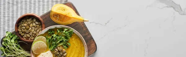 Panoramic shot of autumnal mashed pumpkin soup on wooden cutting board on marble surface — Stock Photo