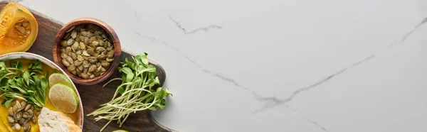 Panoramic shot of autumnal mashed pumpkin soup on wooden cutting board on marble surface with copy space — Stock Photo