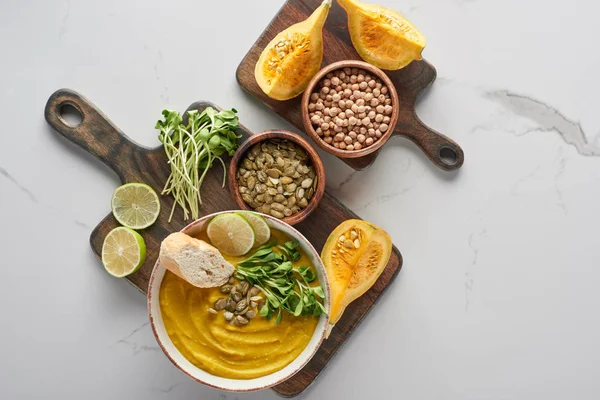 Top view of delicious mashed pumpkin soup on wooden cutting board on marble surface with ingredients — Stock Photo