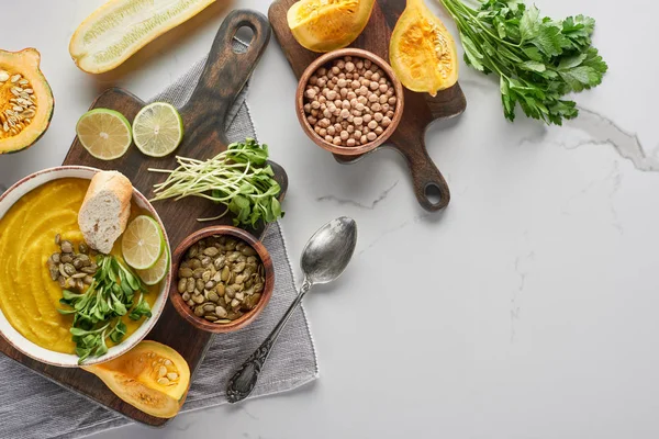 Draufsicht auf köstliche pürierte Kürbissuppe auf Holzschneidebrett auf Marmoroberfläche mit Zutaten — Stockfoto