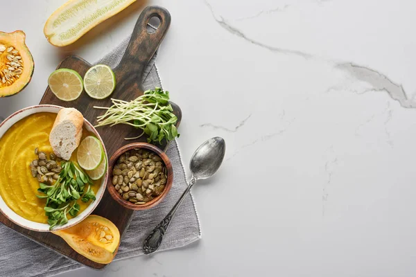 Vista superior da deliciosa sopa de abóbora purê na placa de corte de madeira na superfície de mármore com ingredientes — Fotografia de Stock